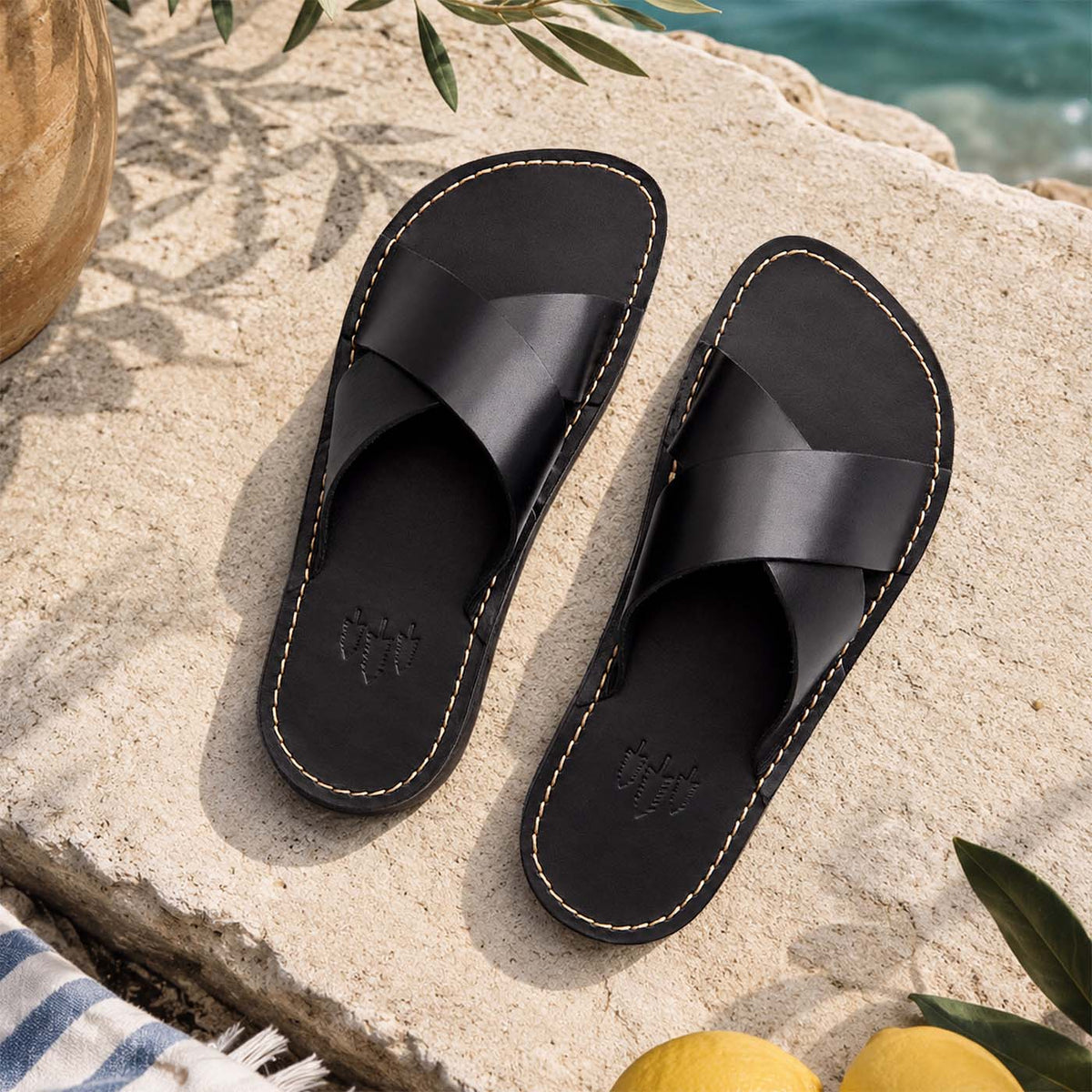 Nero | Black leather flat sandals against a beach background
