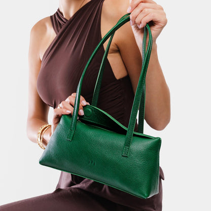 Bacalar | Woman holding a dark green leather bowler bag against a white background