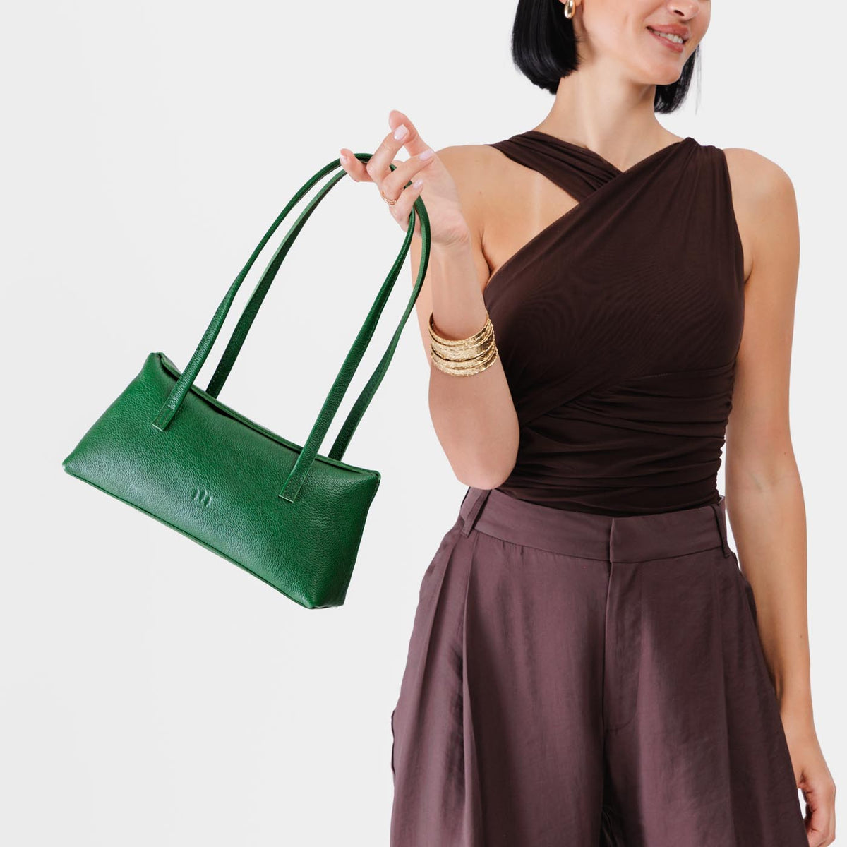 Bacalar | Woman holding a dark green leather bowler bag against a white background