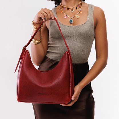 Chili Red*Medium | Model holding u-shaped, flat-bottomed leather shoulder bag with adjustable strap