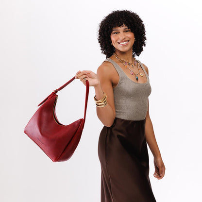 Chili Red*Medium | Model holding u-shaped, flat-bottomed leather shoulder bag with adjustable strap