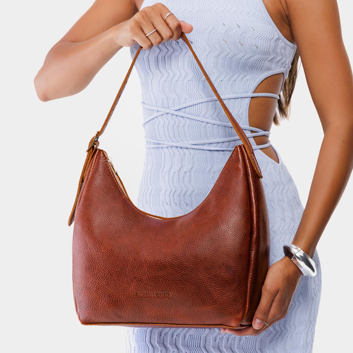 Nutmeg*Medium | Model holding u-shaped, flat-bottomed leather shoulder bag with adjustable strap