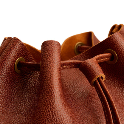 Nutmeg | Close-up of a brown leather drawstring backpack with grommets.
