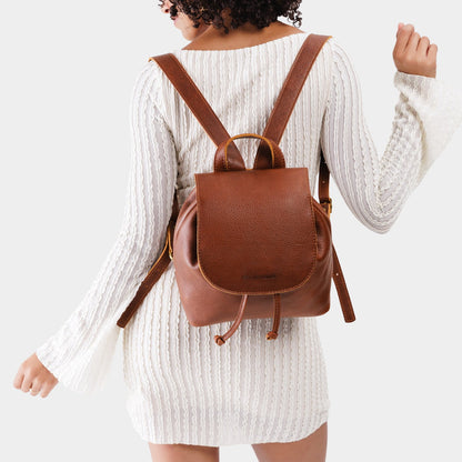 Nutmeg | Pebbled brown leather drawstring backpack being worn by a person wearing a white dress.