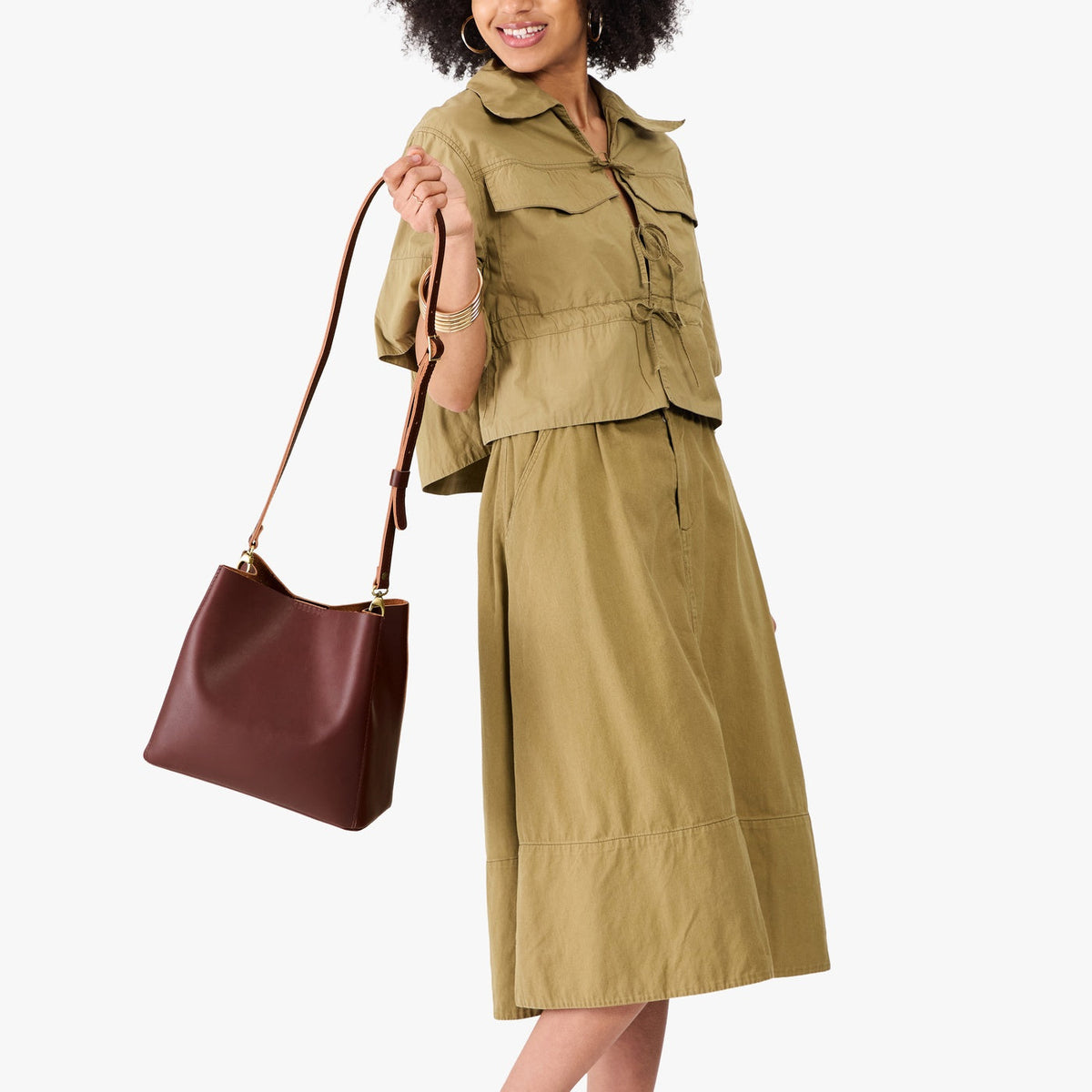 Cognac | Model wearing symmetrical bucket bag with latch closure and removable crossbody strap
