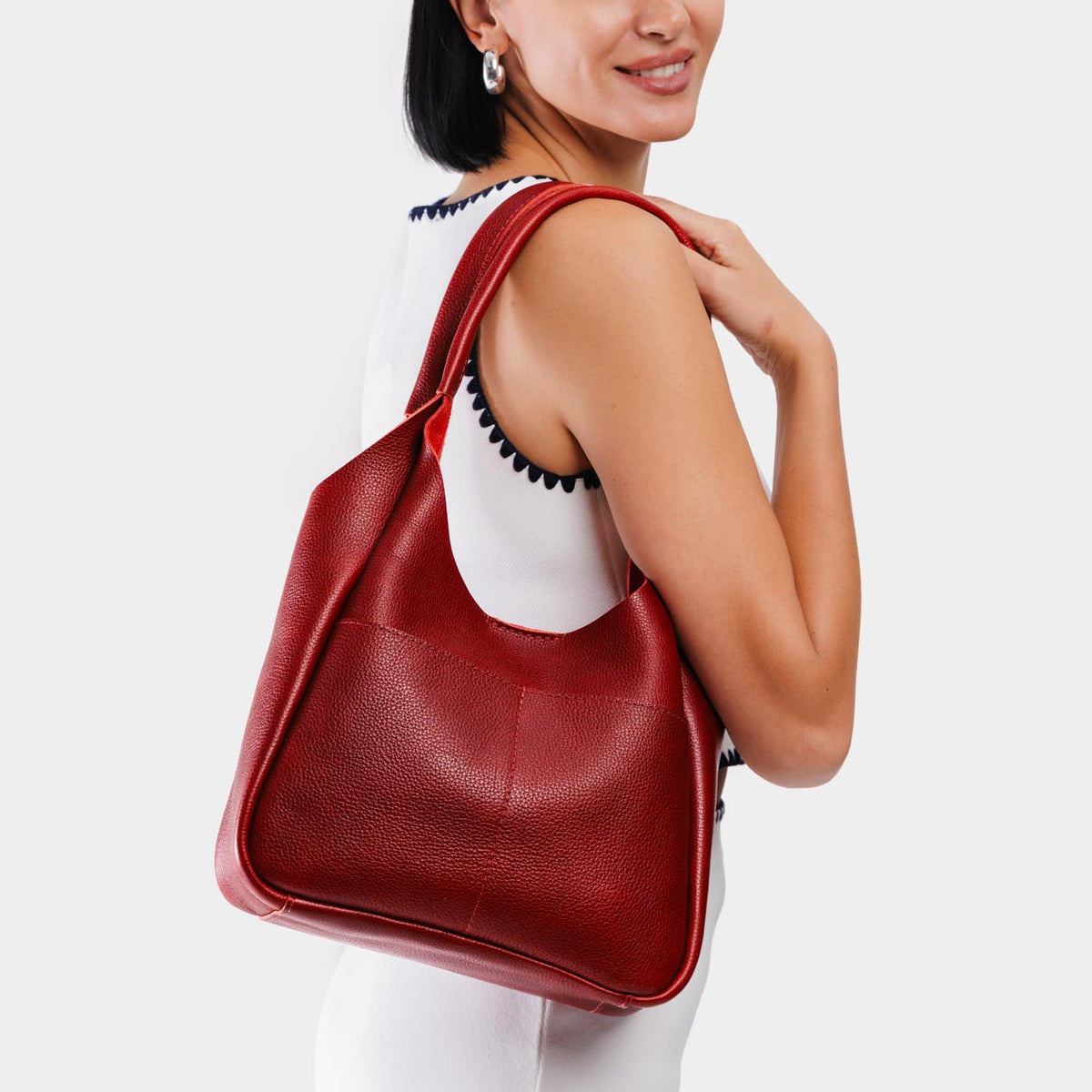 Chili Red*Large | A model holding a u-shaped, flat-bottomed leather shoulder bag with two outside pockets