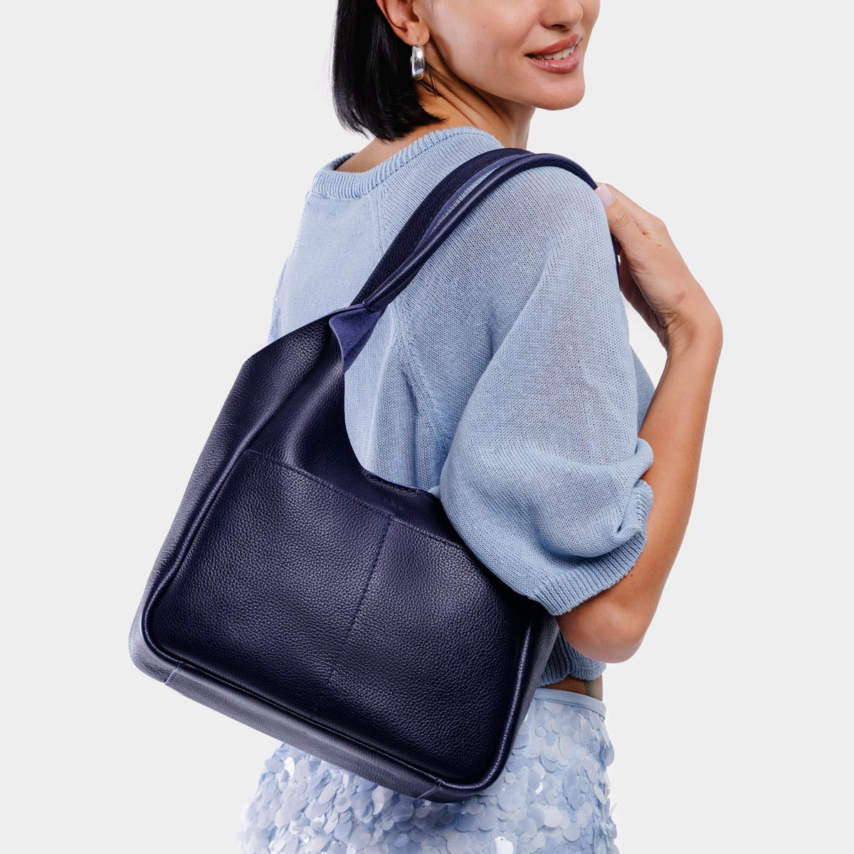 Cobalt*Large | A model holding a u-shaped, flat-bottomed leather shoulder bag with two outside pockets