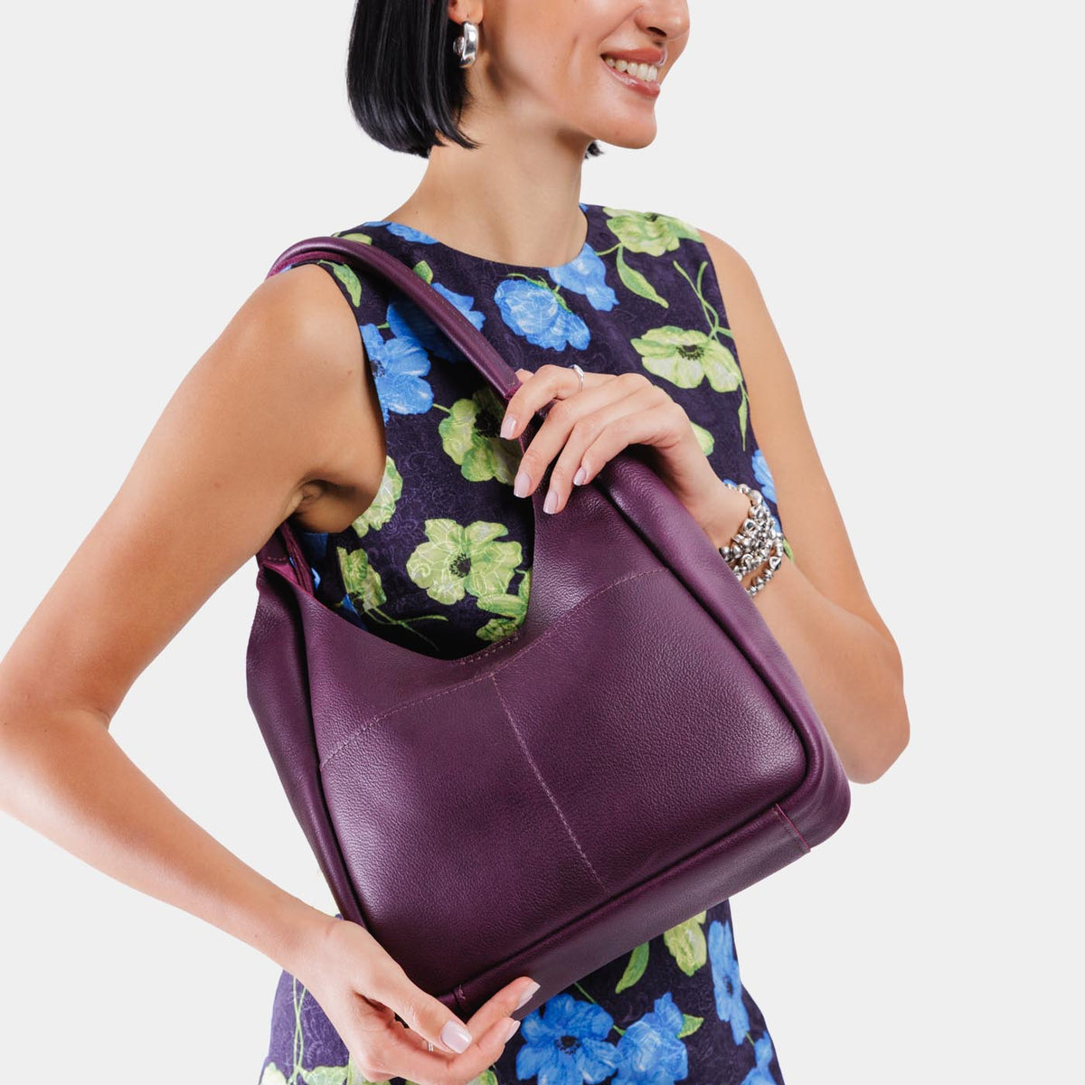 Plum*Large | A model holding a u-shaped, flat-bottomed leather shoulder bag with two outside pockets