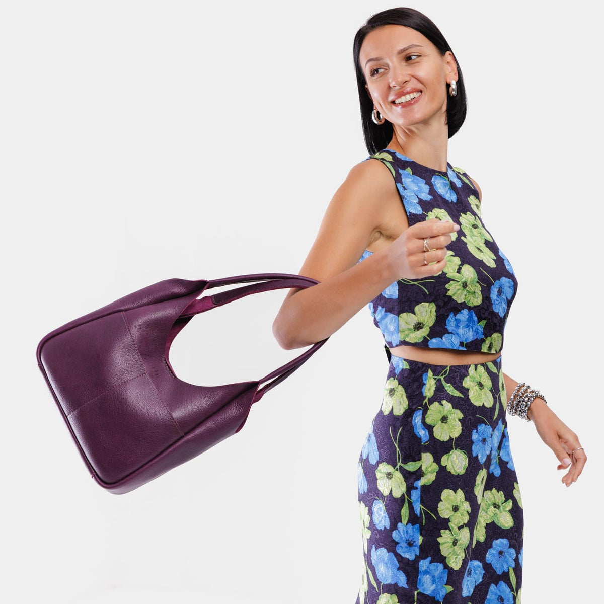 Plum*Large | A model holding a u-shaped, flat-bottomed leather shoulder bag with two outside pockets