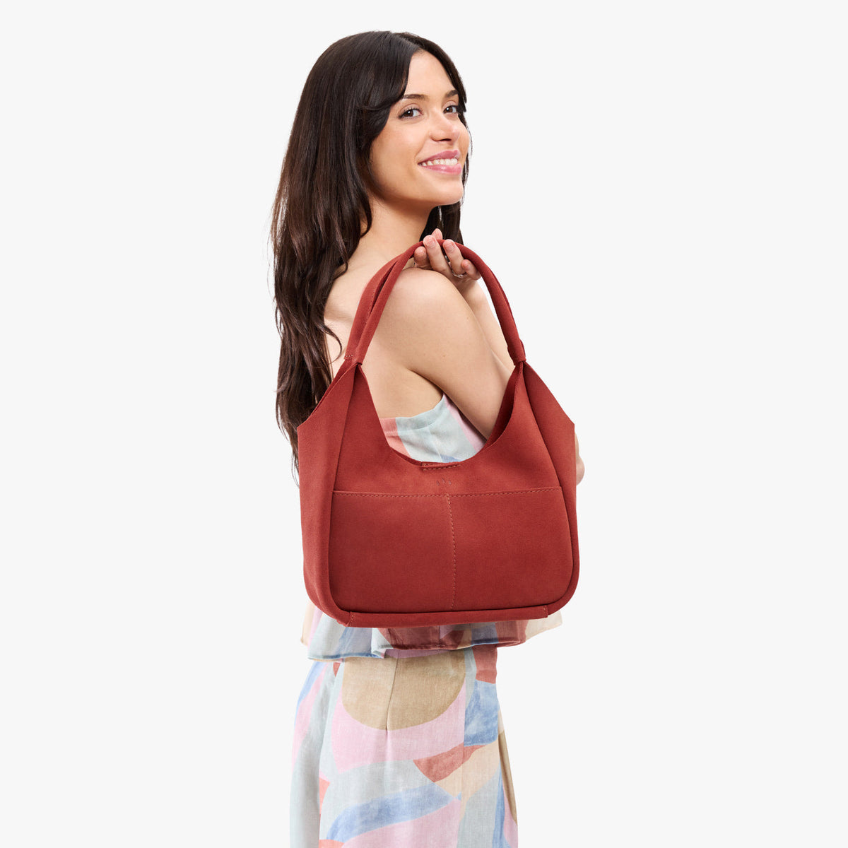 Cinnabar*Medium | A model holding a u-shaped, flat-bottomed leather shoulder bag with two outside pockets