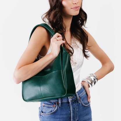 Forest Green*Medium | A model holding a u-shaped, flat-bottomed leather shoulder bag with two outside pockets
