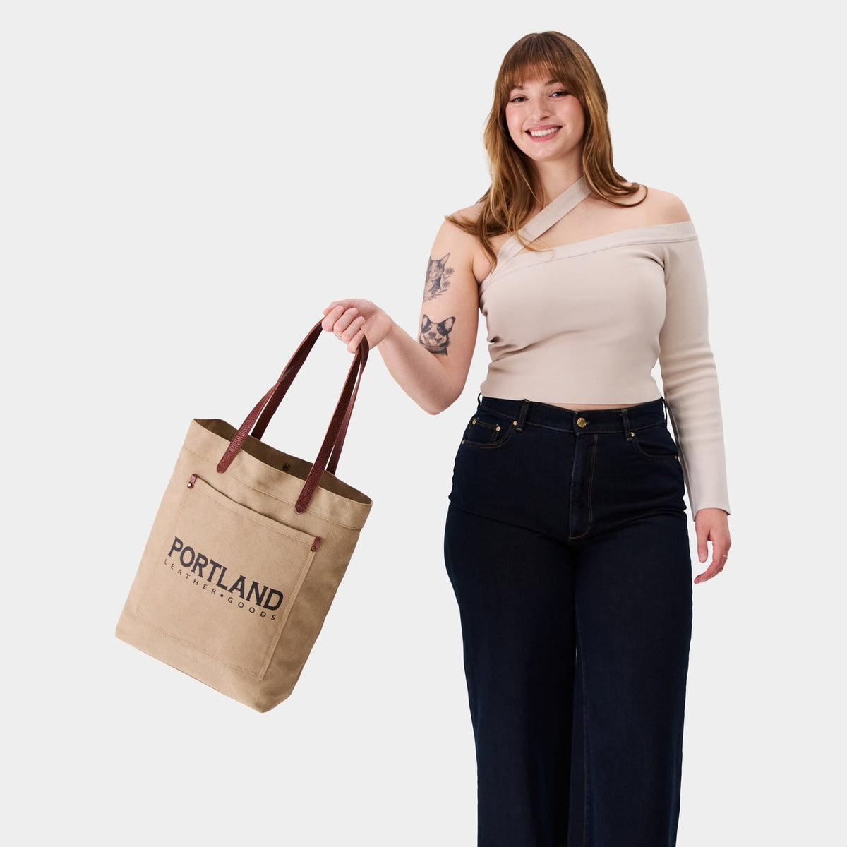Woman holding a canvas tote bag with 'Portland Leather Goods' branding.
